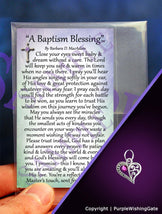 A wallet-size laminated card titled 'A Baptism Blessing,' and a crescent-shaped heart charm with a fuchsia crystal against a purple background.