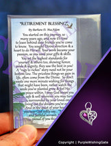 Retirement blessing card and a crescent-shape heart pendant with a fuchsia crystal on a purple background.